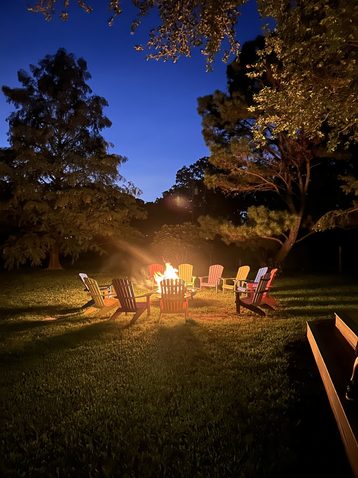 Colorful chairs circled around a campfire under a deep blue evening sky