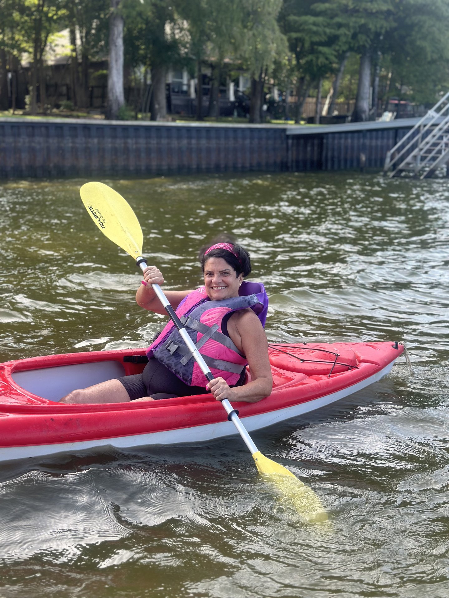 A woman beaming as she paddles a red kayak along the shoreline