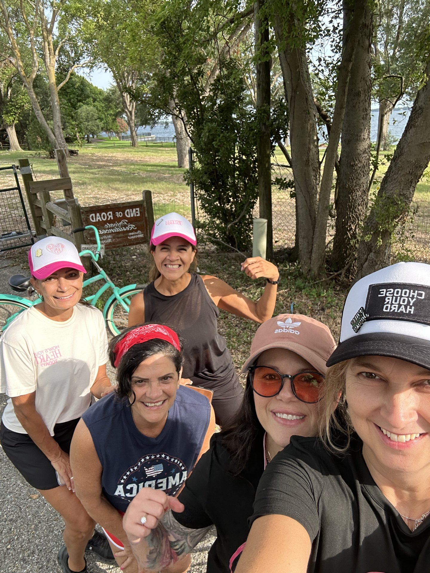 Five women smiling in a selfie beside teal cruiser bikes on a shaded trail